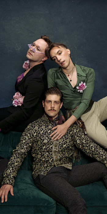 3 people dressed in Renaissance inspired fashions sitting on a velvet couch